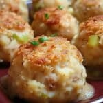 Close-up of several golden-brown mashed potato balls garnished with chopped chives, perfect as a Thanksgiving leftover dish. Arranged on a dark rectangular plate, they're crispy outside with green specks from added herbs or vegetables.