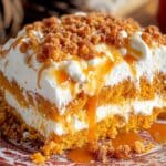 A slice of pumpkin cake with caramel and Heath bits sits on a decorative plate, featuring crumbly topping and creamy filling. The golden-brown base glistens with a caramel drizzle, surrounded by a soft background with hints of warm fall colors.