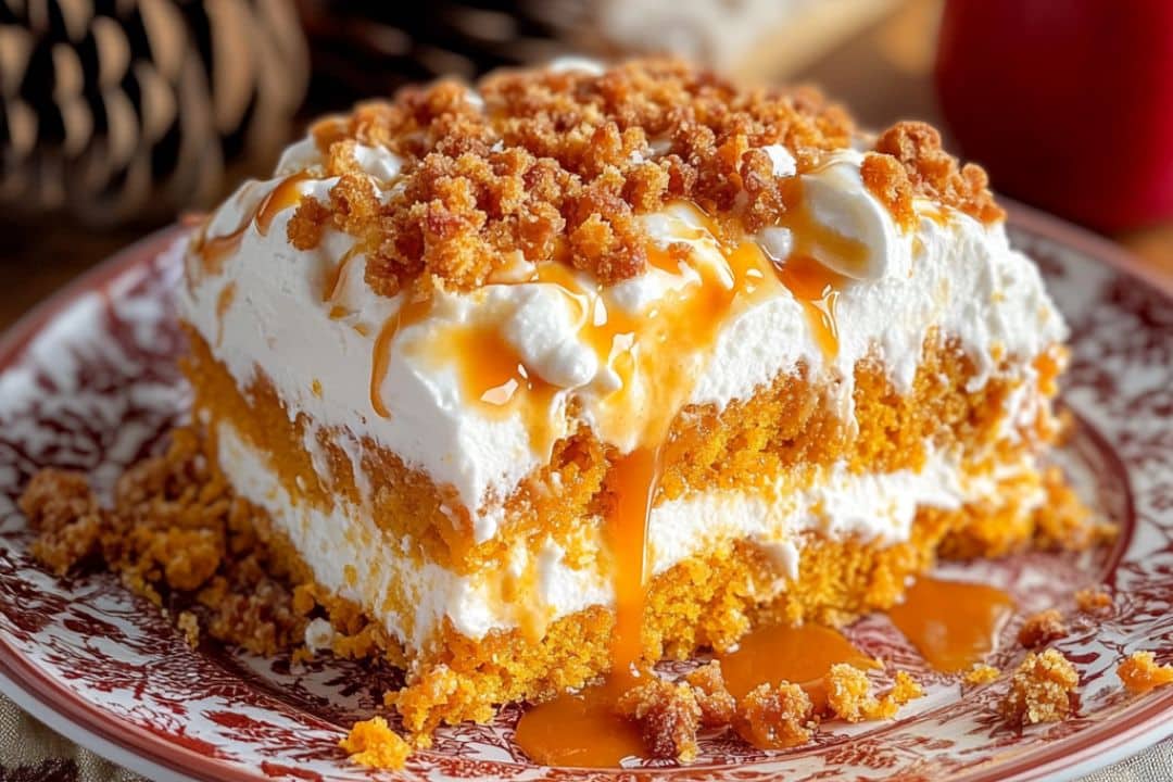 A slice of pumpkin cake with caramel and Heath bits sits on a decorative plate, featuring crumbly topping and creamy filling. The golden-brown base glistens with a caramel drizzle, surrounded by a soft background with hints of warm fall colors.