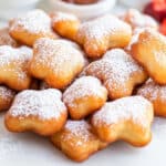 A pile of star-shaped, bite-sized funnel cake beignets sprinkled with powdered sugar rests on a pristine white surface.