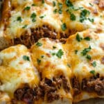 Close-up of cheesy sloppy joes on toasted garlic bread, featuring melted cheese and ground beef, topped with chopped parsley, served on parchment paper.