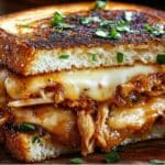 Enjoy a delightful BBQ Chicken Grilled Cheese Sandwich with crispy bread, melted cheese, and shredded barbecue chicken, all garnished with fresh herbs.