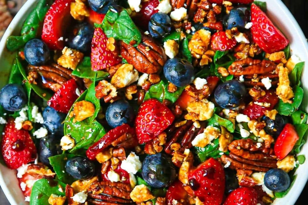 Indulge in a healthy strawberry spinach salad, featuring fresh spinach, juicy strawberries, blueberries, pecans, and crumbled cheese. Drizzled with balsamic glaze, this vibrant dish offers a colorful and appetizing presentation sure to delight your taste buds.