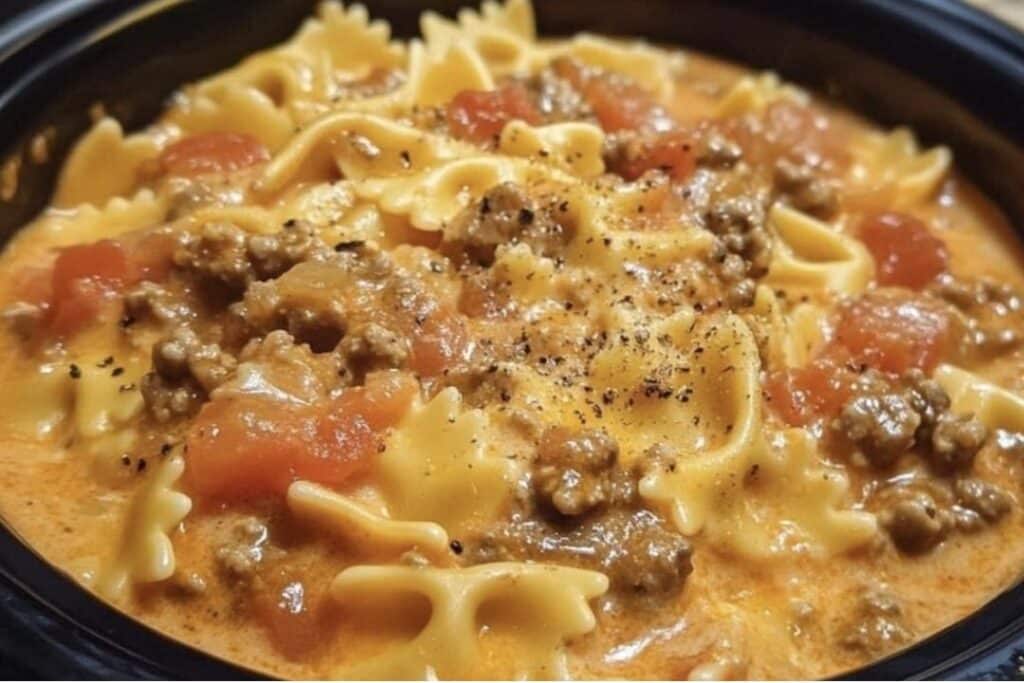 Close-up of a bowl of creamy pot beef and bowtie pasta featuring farfalle noodles, ground meat, and diced tomatoes. The dish is topped with a sprinkling of black pepper—an easy crockpot dinner delight.