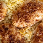 Close-up of a one-pan chicken and rice dish. The baked chicken breasts, seasoned with a golden-brown marinade, rest on fluffy rice. Garnished with minced garlic or onion, the crispy texture of this easy meal adds a delightful touch, making it perfect for any dinner table.