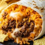 A close-up of an easy burrito recipe filled with melted cheese and seasoned ground beef, with tortilla chips on the side. The burritos tortilla is slightly toasted, highlighting the gooey texture of the cheese and beef mixture.