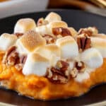 A black dish showcases a sweet potato casserole with marshmallows and pecans, beautifully topped with toasted marshmallows and pecan halves. This delightful creation blends creamy textures with satisfying crunchiness.