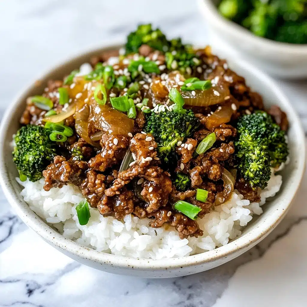 Ground Beef and Broccoli Stir Fry, beef broccoli stir fry recipe, quick weeknight stir fry, easy beef broccoli dish, healthy ground beef stir fry A shallow white bowl holds a two-layer dish: the bottom layer is fluffy white rice, filling the bowl almost to the rim, while the top layer features browned minced beef mixed with glossy, slightly translucent sautéed onions, bright green broccoli florets, and finely sliced green onions. The beef and broccoli mix sits unevenly but generously across the rice, with a sprinkling of white sesame seeds on top for texture. The background and surface are a white marbled texture.