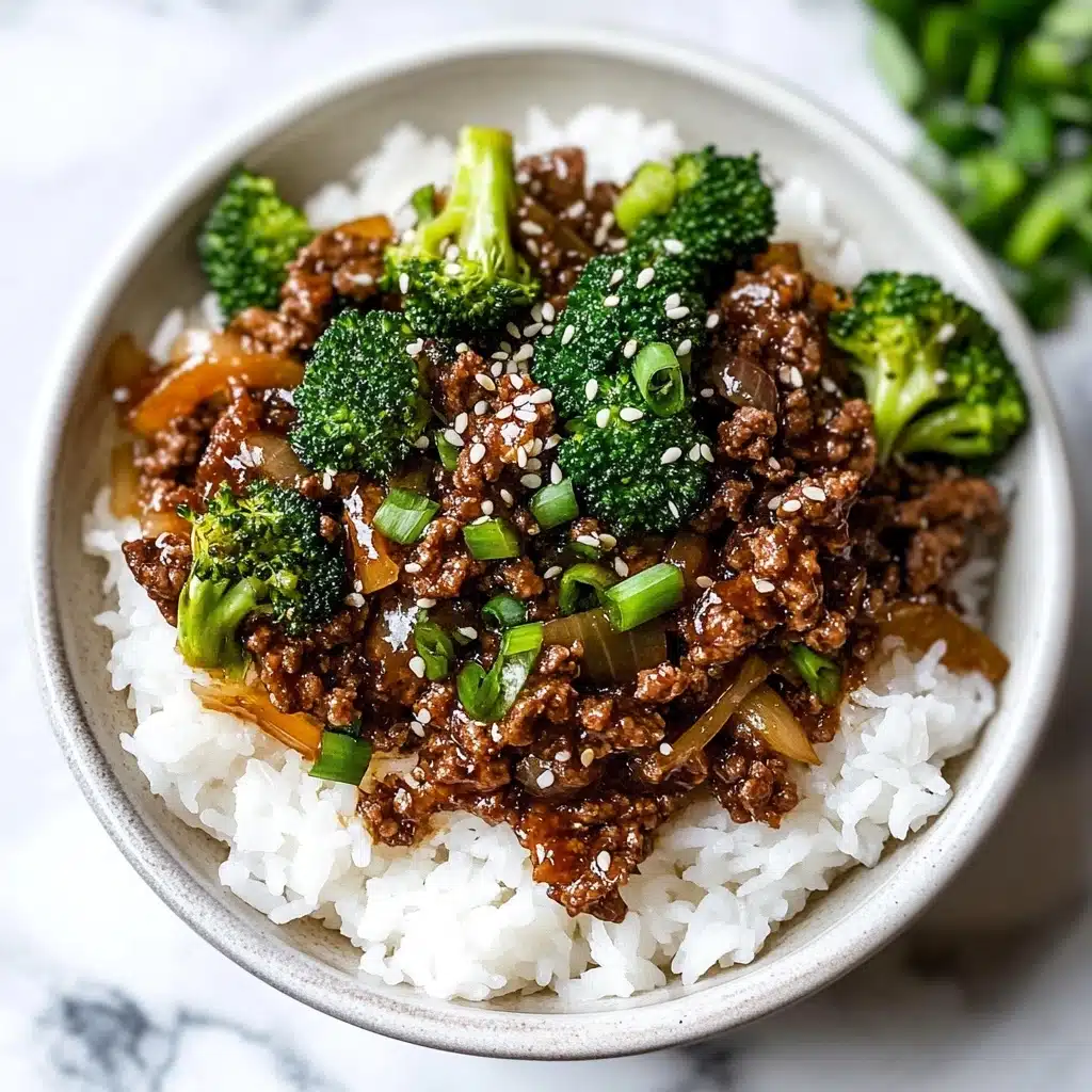 Ground Beef and Broccoli Stir Fry, beef broccoli stir fry recipe, quick weeknight stir fry, easy beef broccoli dish, healthy ground beef stir fry This image shows a pan filled with a cooked dish made of ground beef, bright green broccoli florets, and chunky pieces of translucent white onion. The meat appears brown and crumbly, filling most of the base layer of the pan, while the broccoli and onions are mixed evenly throughout, adding pops of green and off-white color on top and in between the meat pieces. The background surface has a white marbled texture.