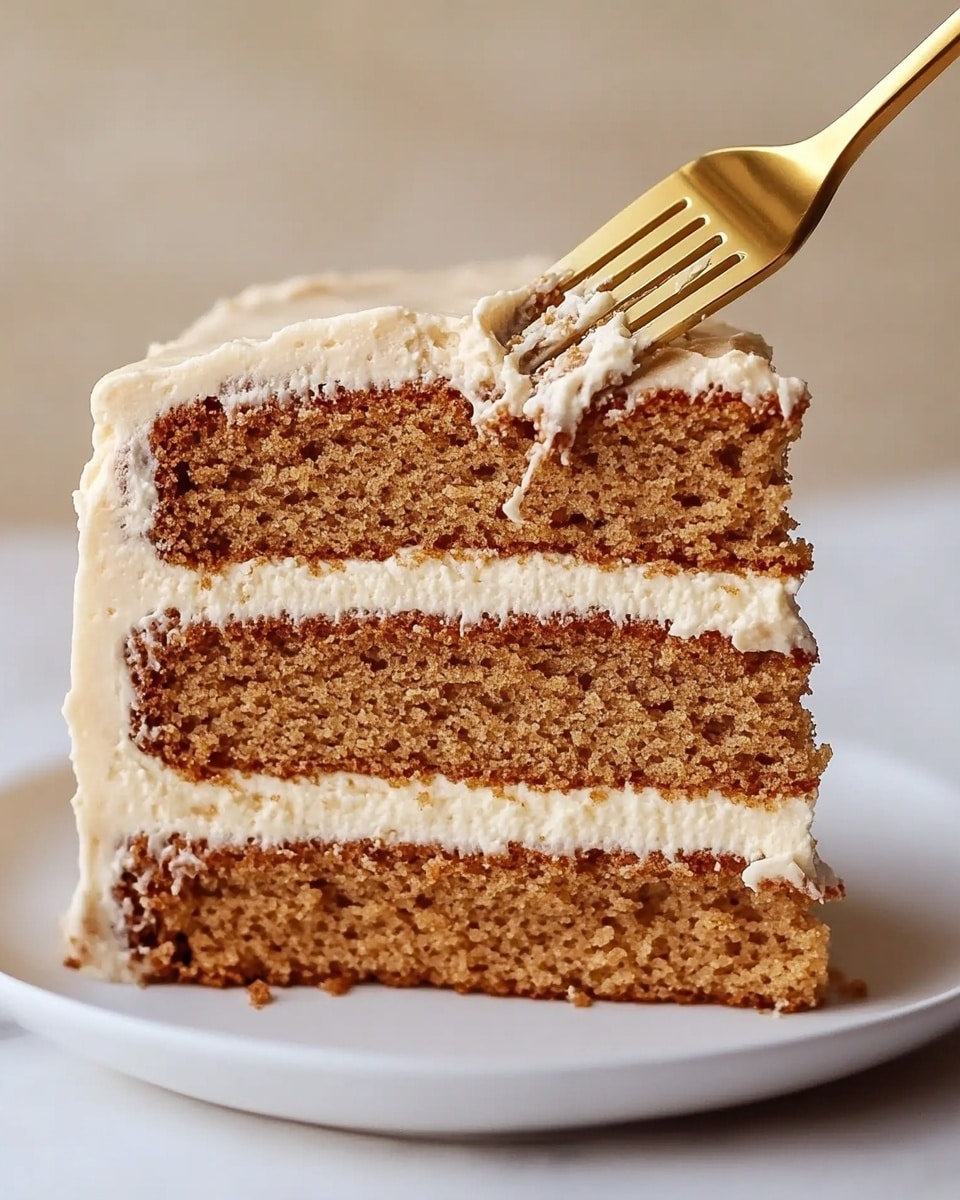 Chai Cake with Brown Butter Cream Cheese Frosting, chai spice cake recipe, cozy fall desserts, homemade chai cake, easy holiday cake A slice of cake with four layers of brown, soft, moist sponge separated by smooth light cream frosting layers. The top layer of the cake is fully covered with the same light cream frosting, slightly textured. A golden fork is digging into the slice, lifting a piece from the middle. The cake sits on a simple white plate placed on a white marbled surface, and the background is out of focus with warm beige tones.