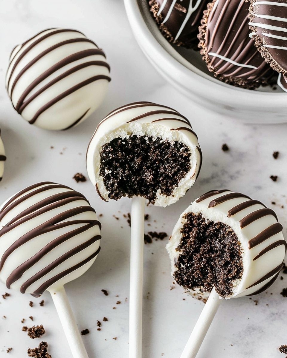 There are five round cake pops, each covered in smooth white coating and drizzled with dark brown chocolate lines on top. One cake pop is shown with a bite taken out, revealing a dark, crumbly inside with white coating around the edge. The cake pops rest on a white marbled surface with small dark crumbs scattered around. In the upper right corner, there is a white bowl filled with stacked, dark chocolate sandwich cookies with white filling. Nearby, three more cookies lie flat on the surface. The whole scene looks clean and bright. Photo taken with an iphone --ar 4:5 --v 6.1
