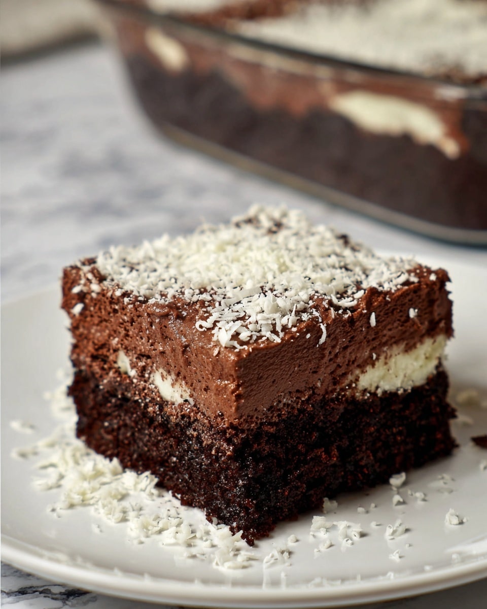 A clear square glass dish holds a thick, dark brown chocolate dessert with a rich, smooth texture. The top layer is sprinkled evenly with fine white shavings, creating a light contrast. One piece is missing from the corner, showing the dense and moist inside of the dessert underneath the white topping. The dish is placed on a white marbled surface. Photo taken with an iphone --ar 4:5 --v 7
