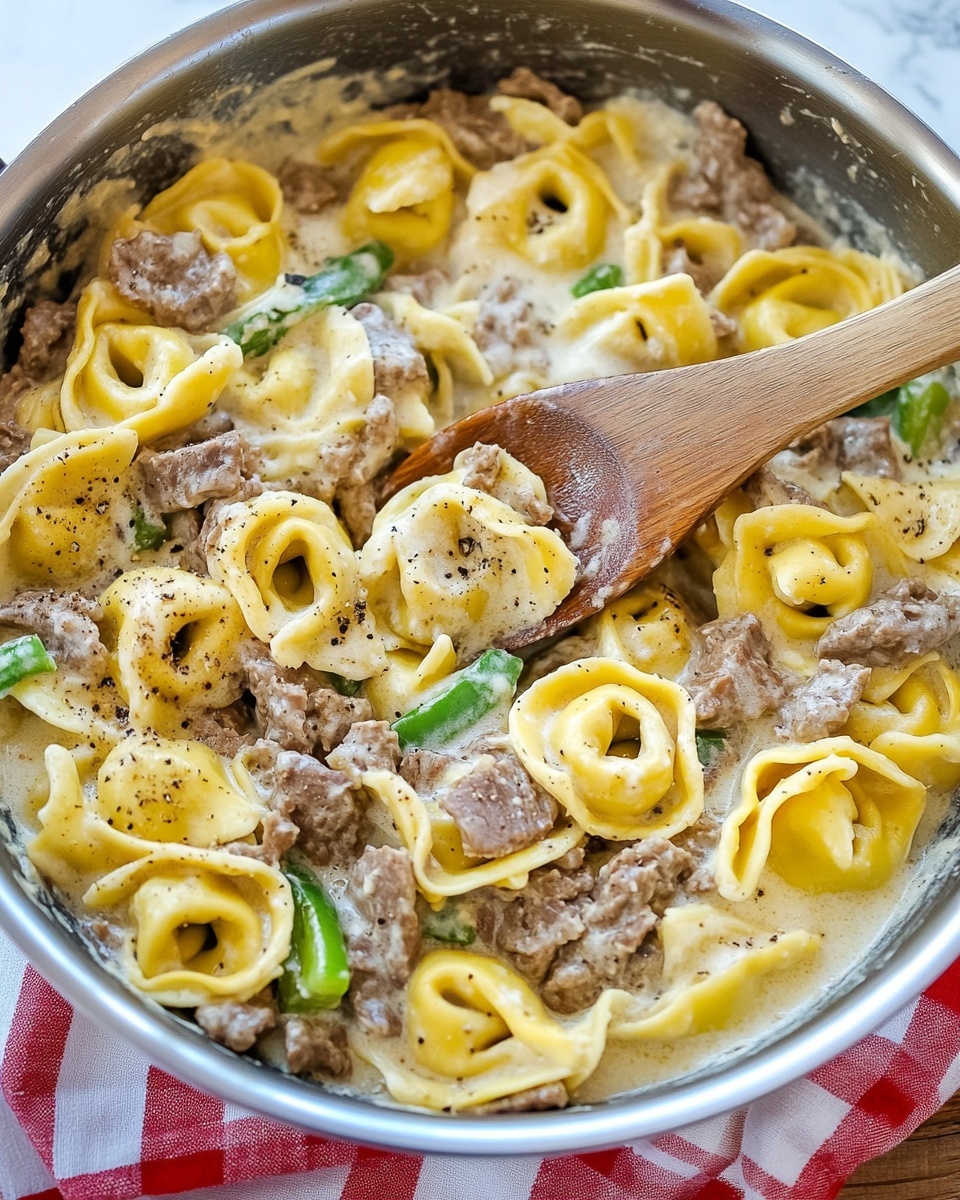 The image shows a silver pan filled with creamy tortellini pasta mixed with small pieces of cooked beef, slices of green bell pepper, and thinly cut onions. The tortellini are golden yellow, covered in a thick white sauce with black pepper specks. In the pan, a wooden spoon is stirring the food, with sauce clinging to it. The pan rests on a wooden surface next to a red and white checkered cloth, but the background is changed to a white marbled texture. Photo taken with an iphone --ar 4:5 --v 6.1
