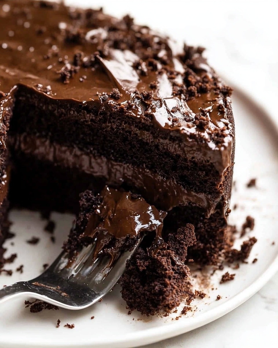 A close-up of a two-layer dark chocolate cake on a white plate, showing a thick, moist texture with melting chocolate chunks between the layers. The top layer is rough and crumbly, with chocolate visibly melting and oozing out. A silver fork is partially inserted into the cake, pressing into the soft top layer. Crumbs and bits of melted chocolate are scattered around the plate on a white marbled surface. photo taken with an iphone --ar 4:5 --v 6.1