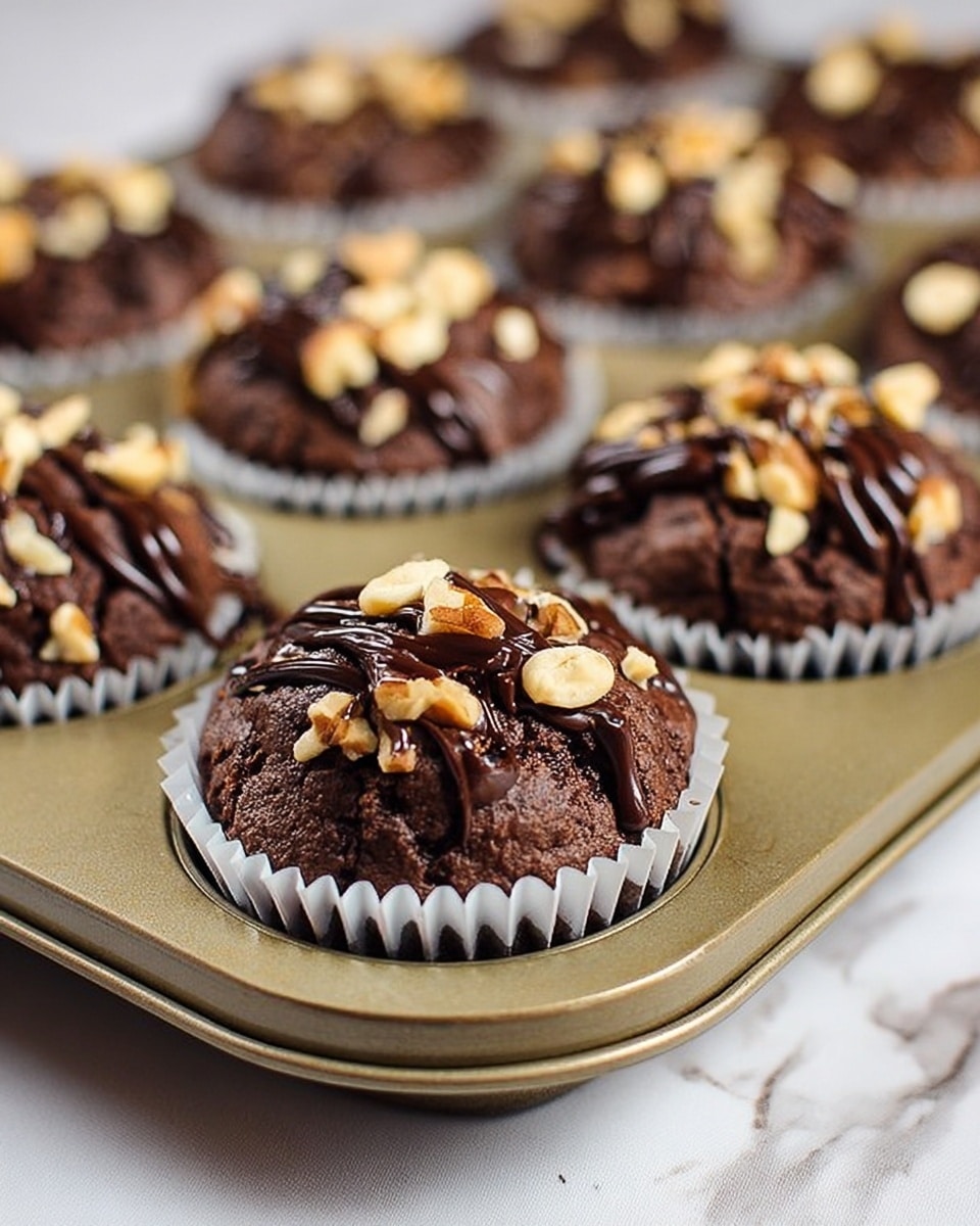 The image shows a tray of chocolate muffins in white paper liners. Each muffin is dark brown and looks soft with a textured top. On top of every muffin, there are pieces of chopped light brown nuts scattered evenly, and a drizzle of glossy dark chocolate sauce covers them in stripes. The metal muffin tray has a pale gold color, and below it is a white marbled surface with soft veins. The focus is on the front muffins, while the others behind are softly blurred. photo taken with an iphone --ar 4:5 --v 7