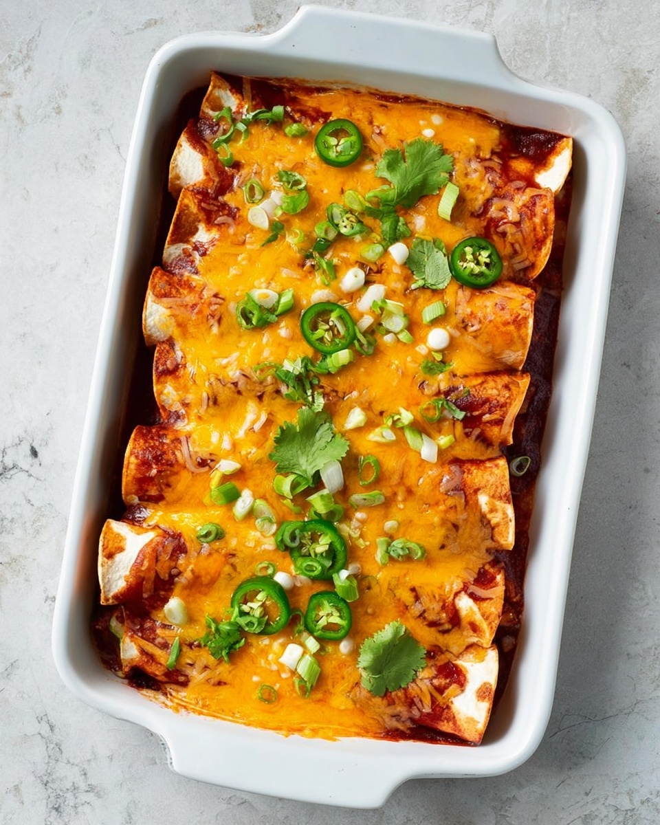 A white rectangular baking dish filled with a layer of rolled tortillas covered by a rich red sauce, topped with a thick, melted layer of bright orange and light yellow cheddar cheese, garnished with fresh green cilantro leaves and slices of green jalapeno peppers, alongside small chopped green onion pieces scattered evenly on top. The dish is set on a white marbled surface. Photo taken with an iphone --ar 4:5 --v 7