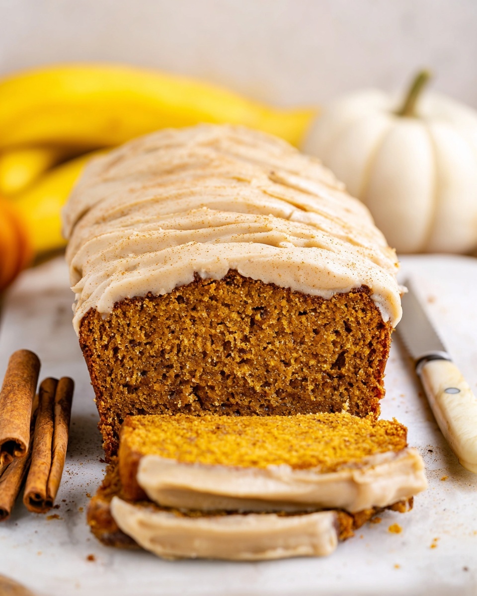 The image shows a loaf of moist pumpkin bread sliced into thick pieces, each slice revealing a dense, orange-brown crumb with small specks throughout. On top of the bread, there is a thick, creamy layer of pale beige frosting with a lightly textured surface, dusted with a fine layer of cinnamon or spice powder. The loaf is placed on a white marbled texture surface, with two cinnamon sticks lying in front, and two yellow bananas and a small white pumpkin blurred in the background. A knife with a white handle is seen on the right side of the image resting on the white marbled texture. photo taken with an iphone --ar 4:5 --v 7