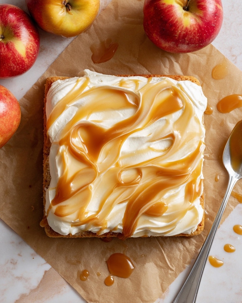 A square dessert with two layers on a piece of brown parchment paper: the bottom layer is a light brown soft cake with a slightly uneven edge, and the top layer is thick white cream spread evenly. Over the cream is a shiny caramel swirl spread in waves, blending light and dark golden tones. Around the dessert, there are small drops and smears of caramel sauce on the paper. In the top right corner, there are three red apples with yellow spots. In the bottom right corner, a silver spoon with caramel sauce on it rests on the paper, and a white marbled surface is visible underneath. photo taken with an iphone --ar 4:5 --v 7
