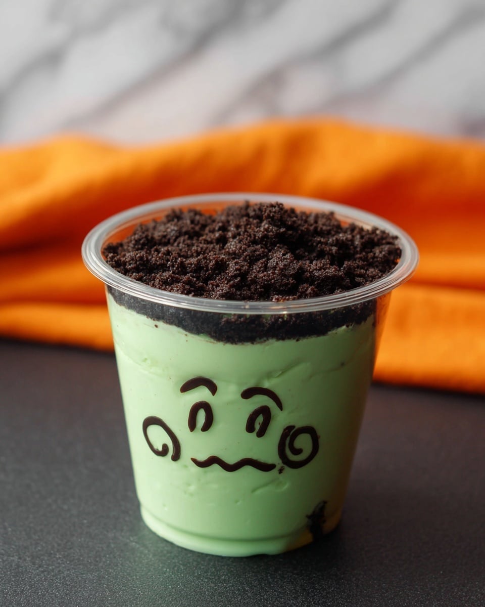 The image shows four clear plastic cups filled with two layers: the bottom layer is a smooth, light green pudding, and the top layer is a dark, crumbly chocolate cookie crumble that looks like hair. Each cup has a cute, cartoonish face drawn on the outside, with different expressions using black marker. In the foreground, a woman's hand is holding one cup with a happy face, while the other three cups with varied faces are placed in the background on a white marbled surface, with an orange cloth partially visible. photo taken with an iphone --ar 4:5 --v 7