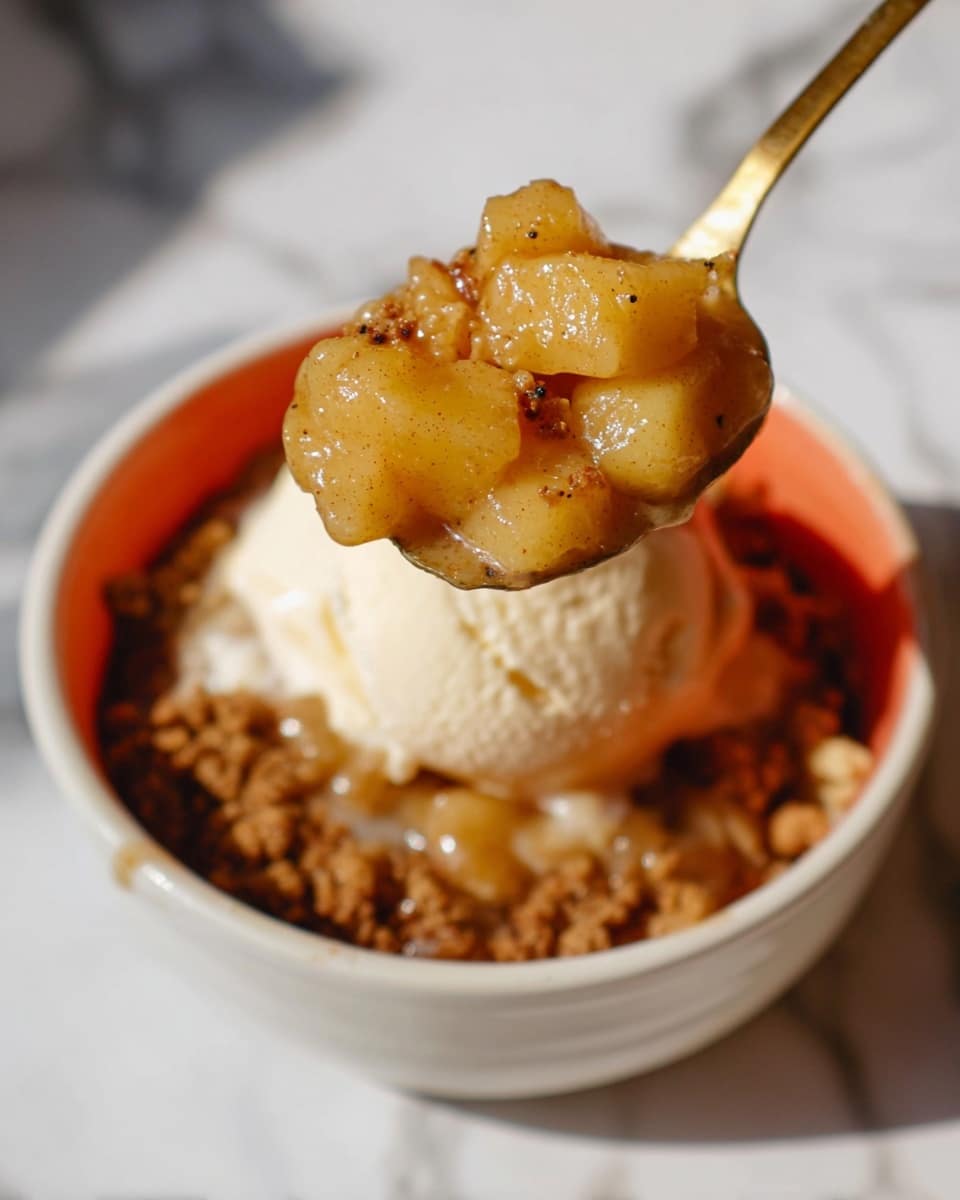 A close-up view of a dessert in a white bowl with an orange interior, placed on a white marbled surface. The dish has three layers: the bottom layer is a crumbly brown crust, the middle layer consists of soft, cooked apple pieces with a shiny, syrupy glaze and small dark specks of cinnamon, and the top layer is a scoop of a light cream or ice cream, slightly melting. A golden spoon holds a scoop with several apple chunks, suspended above the bowl. The photo has warm lighting and soft shadows, highlighting the texture of the apples and crumbly crust photo taken with an iphone --ar 4:5 --v 7