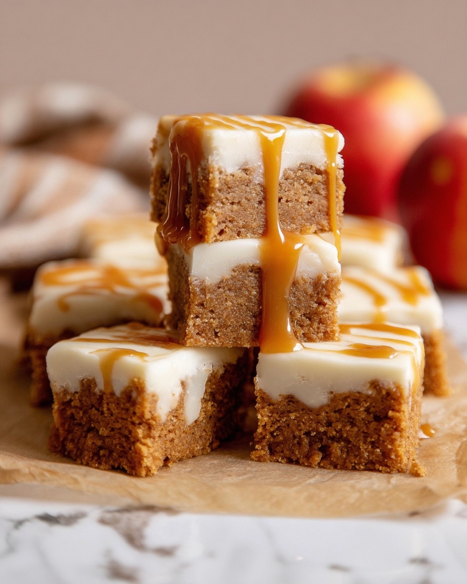 The image shows several small square cake pieces stacked together on a light brown paper, placed over a white marbled surface. Each piece has two visible layers: the bottom layer is a brown, crumbly cake with a soft texture, and the top layer is a smooth, creamy white icing. One cake piece is stacked vertically on top of another, with a golden caramel sauce dripping down from the icing. In the background, partially blurred, there are two red apples. The overall color palette is warm and inviting with natural lighting. Photo taken with an iphone --ar 4:5 --v 7