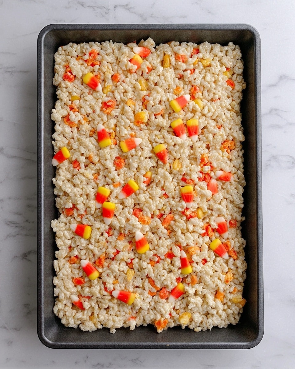 A rectangular pan filled with one thick layer of light beige puffed rice cereal tightly packed together, mixed with small scattered pieces of candy corn with bright orange, yellow, and white colors throughout. The pan is dark gray and sits on a white marbled surface. The overall texture looks soft and chewy. photo taken with an iphone --ar 4:5 --v 7