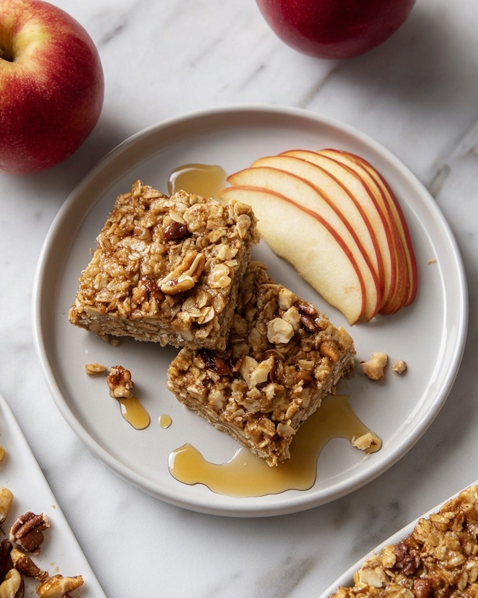 A thick square slice of oatmeal bake sits on a white plate with a white marbled surface underneath. The top layer is a mix of golden toasted oats, small chunks of light brown apples, and whole pecans, scattered unevenly with a sticky shine from syrup. The bottom layer is a dense, beige cooked oatmeal base with a soft, moist texture. Some syrup pools on the plate around the slice, adding a glossy look. A couple of thin apple slices lean against the back of the oatmeal piece on the plate. photo taken with an iphone --ar 4:5 --v 7