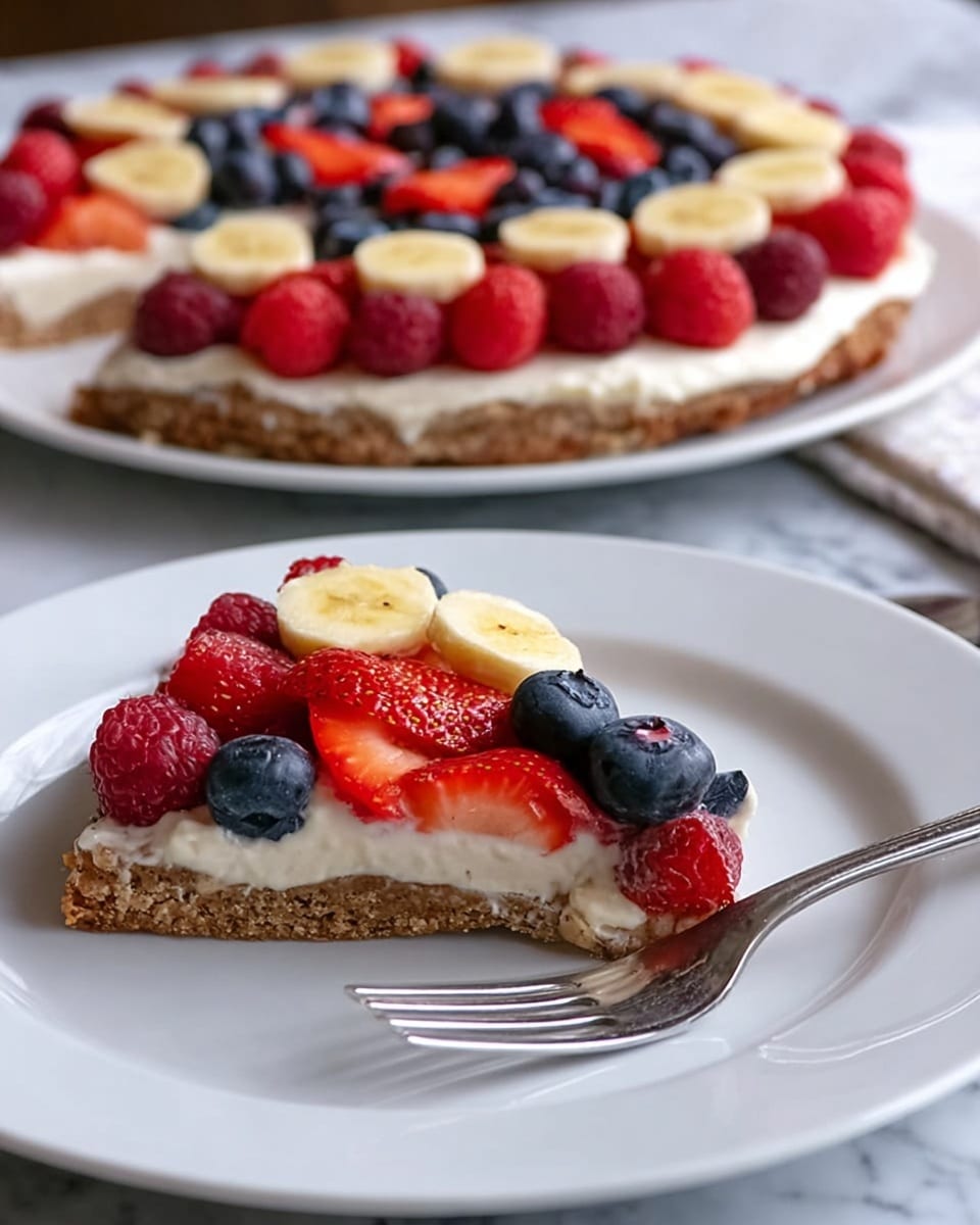 The image shows a slice of fruit pizza on a white plate with a silver fork beside it. The fruit pizza has three layers: a brown crust at the bottom with a slightly rough texture, a thick white creamy layer in the middle, and a colorful fruit topping arranged on top. The fruit layer includes bright red strawberry slices placed along the edge, dark red raspberries, dark blue blueberries, and round yellow banana slices spread evenly across the creamy layer. In the background, there is the remaining portion of the fruit pizza on a larger white plate, sitting on a white marbled surface. Photo taken with an iphone --ar 4:5 --v 7