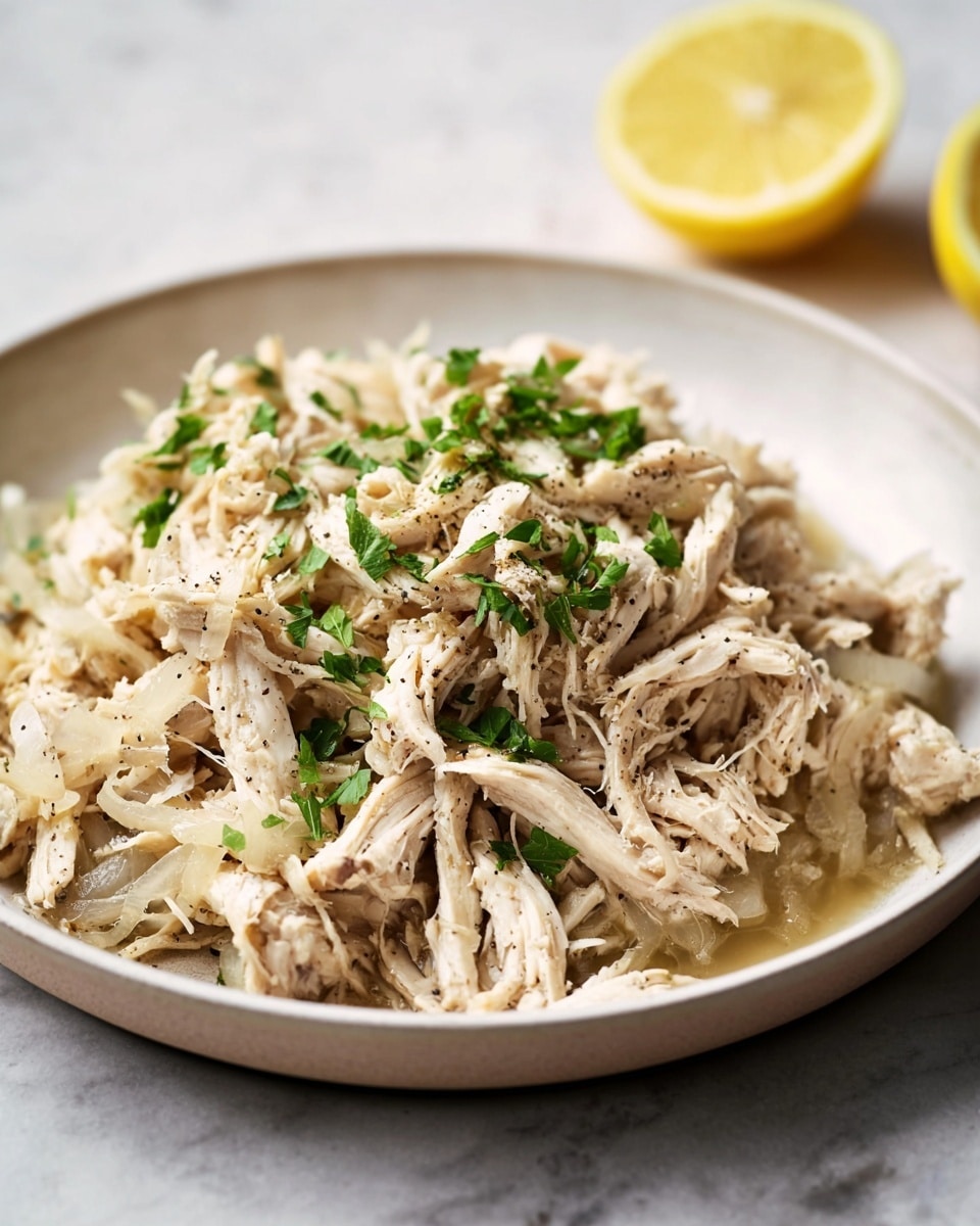 A white bowl filled with a single layer of shredded cooked chicken that is light beige in color, mixed with soft translucent cooked onion slices scattered throughout. The chicken is covered with a light brown sauce that has a slightly glossy texture, and the dish is topped with a sprinkle of black pepper and fresh chopped green herbs, adding a pop of color. The entire bowl is placed on a white marbled surface, with a blurred hint of a lemon in the top right corner. photo taken with an iphone --ar 4:5 --v 7
