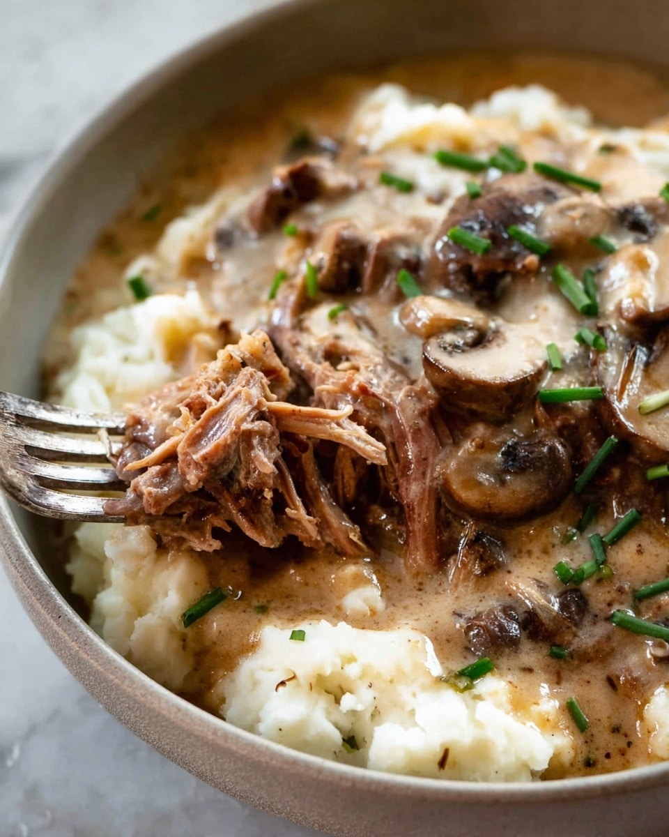 This close-up image shows a creamy dish in a white bowl on a white marbled surface. The dish has three main layers: the bottom layer is soft mashed potatoes in white color and fluffy texture. The middle layer consists of brown shredded meat being lifted slightly by a silver fork, showing tender and fibrous texture. The top layer is a light brown creamy sauce with sliced cooked mushrooms and small green chives sprinkled on top. The sauce appears smooth and rich, covering the meat and mashed potatoes partly. Photo taken with an iphone --ar 4:5 --v 7