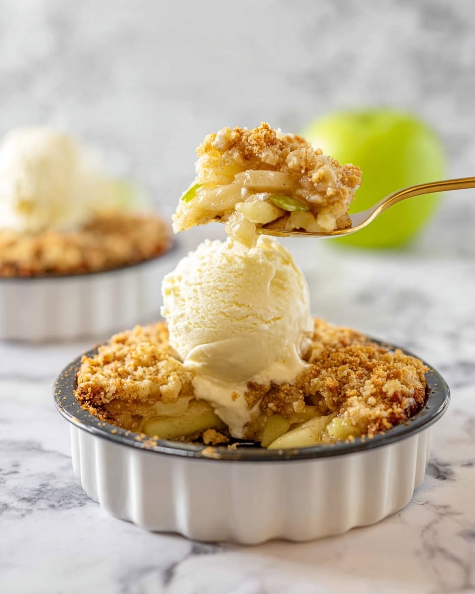 The image shows a round dessert with three visible layers: the bottom layer is a light brown, slightly crumbly crust; the middle layer contains golden, soft apple slices mixed with small bits of apple; the top layer is a crumbly, golden streusel with a rough textured surface. A scoop of creamy white ice cream sits on top of the dessert in a white dish with scalloped sides. A golden spoon holding a bite of the dessert and ice cream is raised above it, and a green apple is blurred in the white marbled background behind. photo taken with an iphone --ar 4:5 --v 7