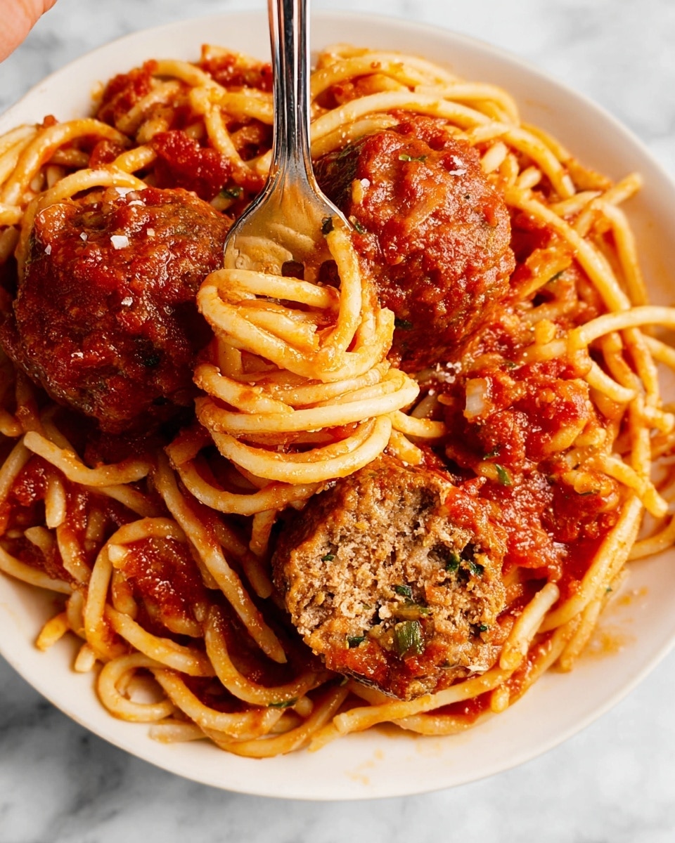 A close-up view of a white plate with spaghetti and large meatballs in tomato sauce. The spaghetti is light golden with a smooth, slightly shiny texture, twisting and looping around a silver fork held by a woman's hand near the top left. The tomato sauce is rich red with visible small chunks, covering the bottom and coating the spaghetti. There are two large meatballs, one whole and one cut in half showing a dense, slightly crumbly brown interior with green and white bits. The white plate sits on a white marbled surface. photo taken with an iphone --ar 4:5 --v 7
