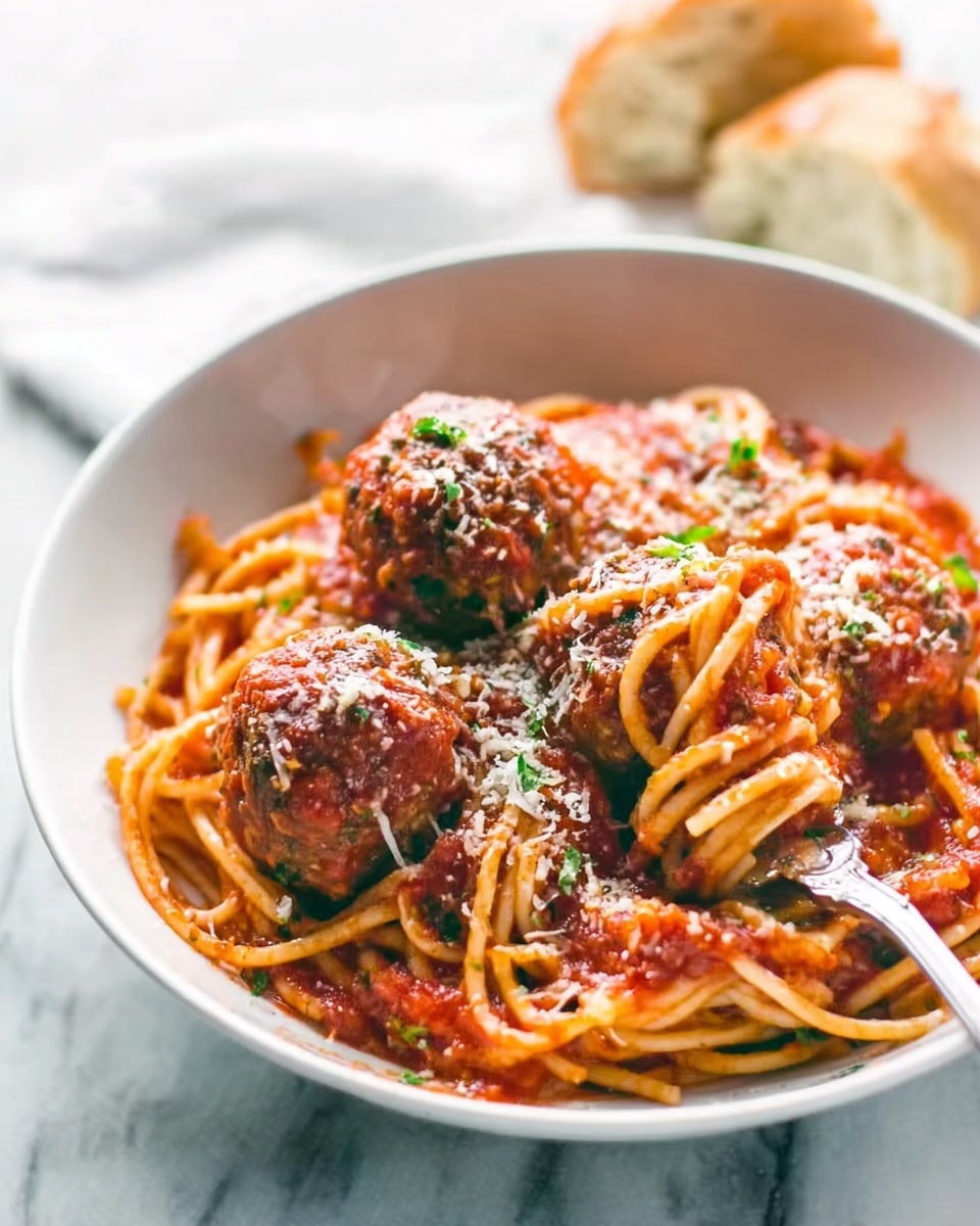 Spaghetti and Meatballs Recipe 6 A white bowl filled with spaghetti covered in red tomato sauce, topped with three large brown meatballs sprinkled with grated white cheese and small green herb bits. A silver fork rests inside the bowl on the right side, curling some noodles. The background shows a white marbled surface with some bread in soft focus. The image is bright and clear, capturing the textures of the sauce, meatballs, and cheese. Photo taken with an iphone --ar 4:5 --v 7