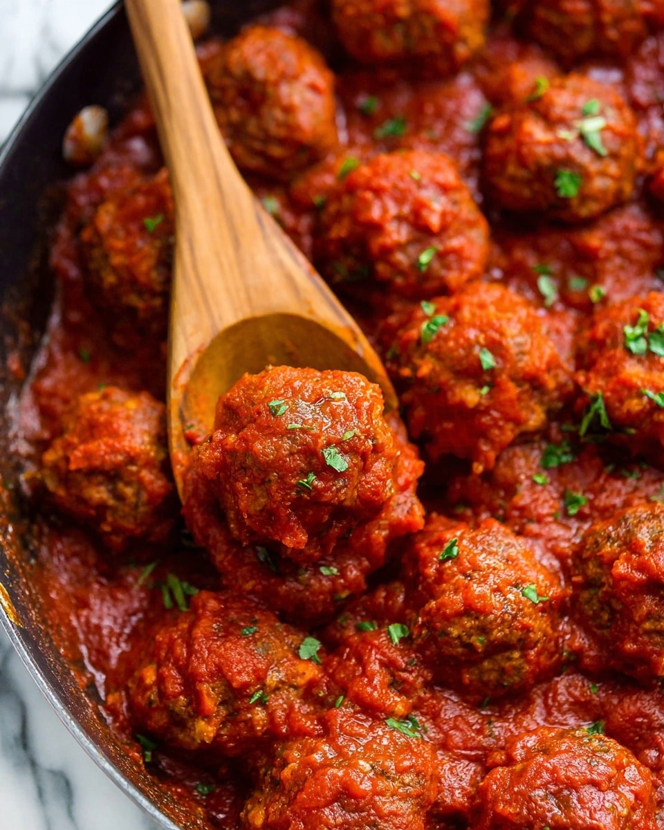 Classic Homemade Meatballs Recipe 5 The image shows many round meatballs covered with a thick red tomato sauce, arranged close together in a pan. The meatballs have a slightly rough texture and are garnished with small green herb pieces scattered on top. A wooden spoon is lifting one meatball, revealing its shape and sauce coating clearly. The background has a white marbled texture. photo taken with an iphone --ar 4:5 --v 7