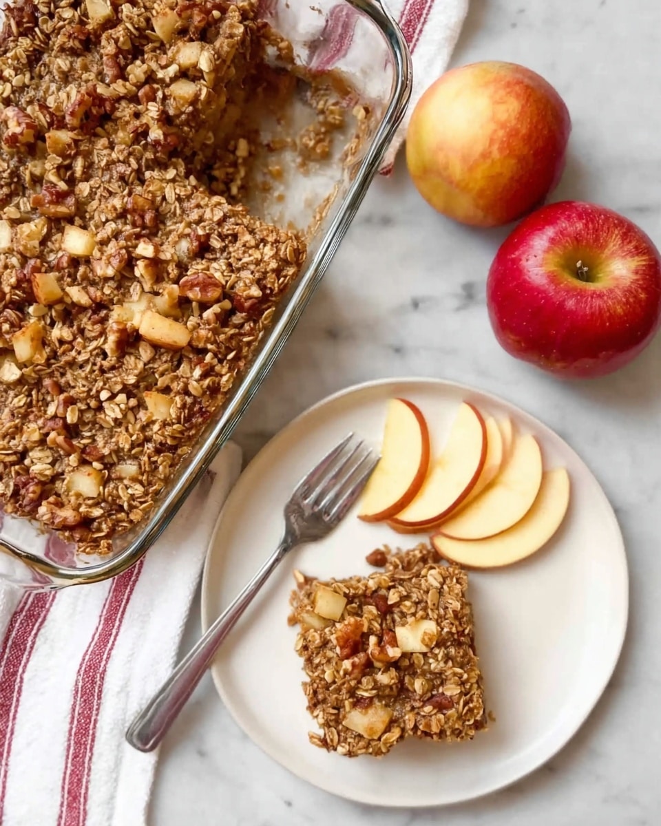 A square glass baking dish filled with a golden brown oat and nut mixture, showing a rough, bumpy texture with visible chunks of nuts and small pieces of apple on top. On a white marbled surface beneath, there's a white plate with a thick square piece of the oat dish sitting on it, next to three thin, pale yellow apple slices with red edges arranged to the side. A silver fork rests on the plate next to the oat piece. Nearby on the white marbled surface, two whole apples, one red and one red-yellow, are placed beside the dish and plate. A white cloth with red stripes peeks out from under the baking dish. photo taken with an iphone --ar 4:5 --v 7