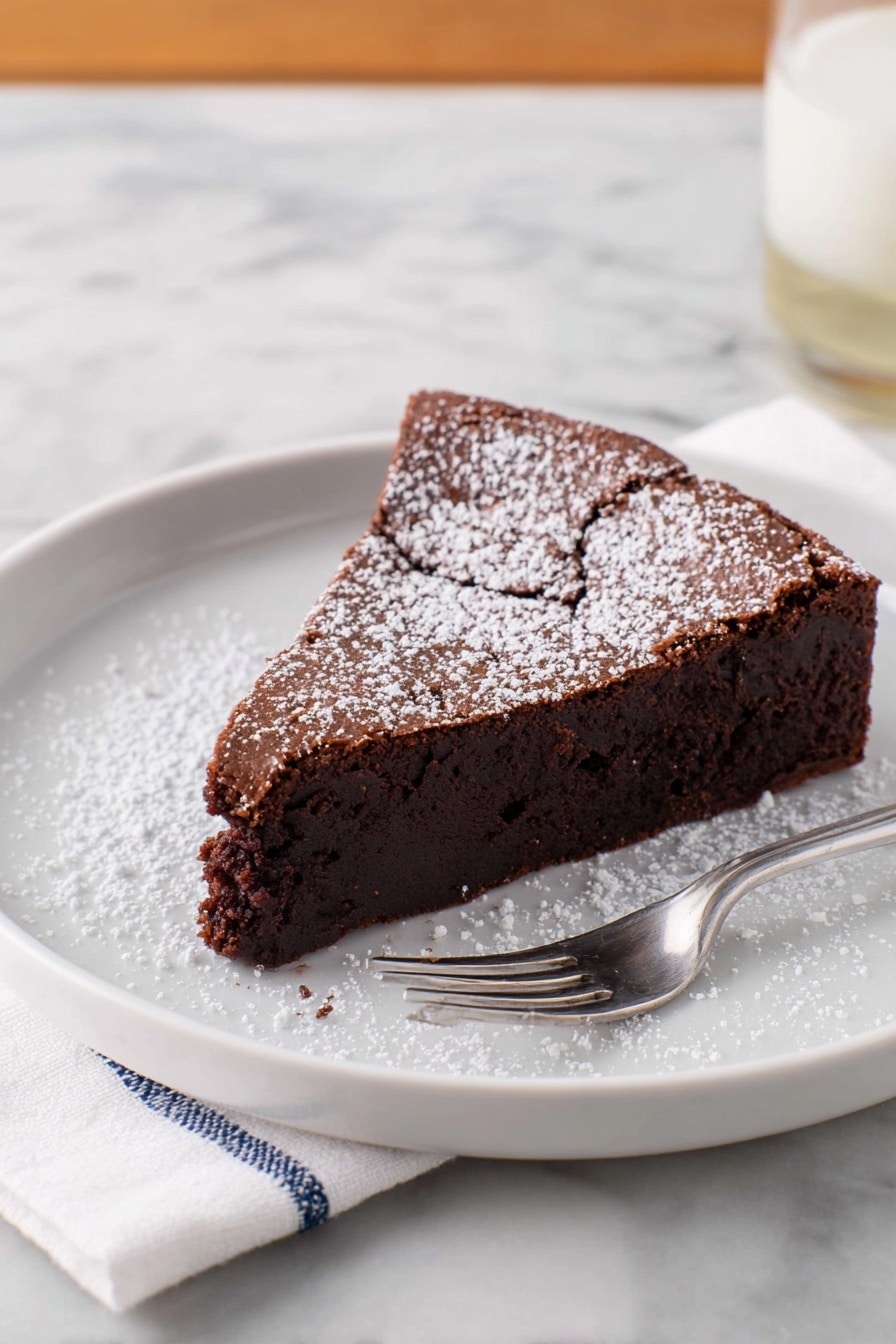 A single slice of dark brown chocolate cake with a slightly cracked top layer is placed on a white plate. The cake has one thick layer that looks moist and dense, dusted with a light sprinkle of white powdered sugar on top and around the plate. A silver fork rests on the plate next to the cake. The plate sits on a white marbled surface with a white napkin with blue stitching beside it. Photo taken with an iphone --ar 2:3 --v 7 - Flourless Chocolate Torte, gluten-free chocolate dessert, decadent chocolate cake, easy chocolate tart, rich chocolate dessert