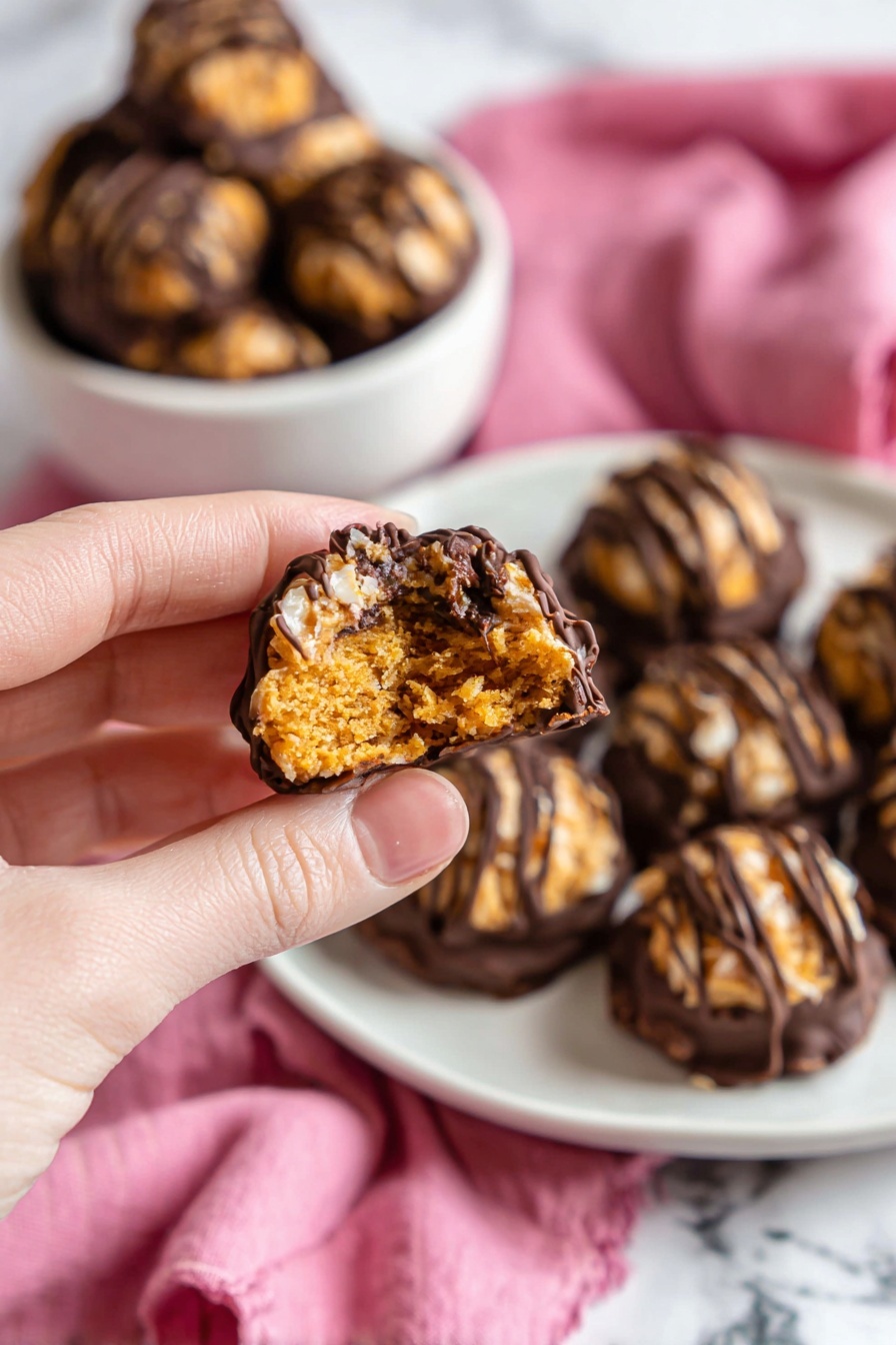 Samoa Coconut Truffles Recipe 6 A close-up of a small round treat held by a woman's hand, showing a textured golden brown top layer with dark chocolate drizzles and a bitten middle that reveals a crumbly, moist interior in shades of golden brown. Below it, a white bowl holds multiple similar treats with the bottom dipped in dark chocolate, and in the back, more treats are stacked on a white plate with a soft pink cloth around them, all placed on a white marbled surface. photo taken with an iphone --ar 2:3 --v 7 - Samoa Coconut Truffles, Samoa Cookies dessert, homemade Samoa truffles, coconut chocolate truffles, no-bake Samoa candies