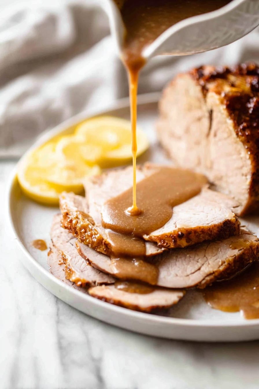 Juicy Slow Cooker Turkey Breast Recipe 8 The image shows a white plate on a white marbled surface with a large piece of cooked meat that has a golden-brown, crispy crust and some green herbs on top. To the right are four thick slices of meat, layered neatly with brown gravy drizzled over them. On the left side of the plate, there are two round lemon slices placed flat and a lemon wedge at the bottom right of the plate. Behind the plate, a white cloth holds a silver knife and fork with black handles, and to the upper left, there is a white gravy boat filled with brown gravy, with a silver spoon resting inside it. Photo taken with an iphone --ar 2:3 --v 7 - Juicy Slow Cooker Turkey Breast, easy turkey dinner recipe, tender turkey breast, slow cooker turkey ideas, holiday turkey recipe