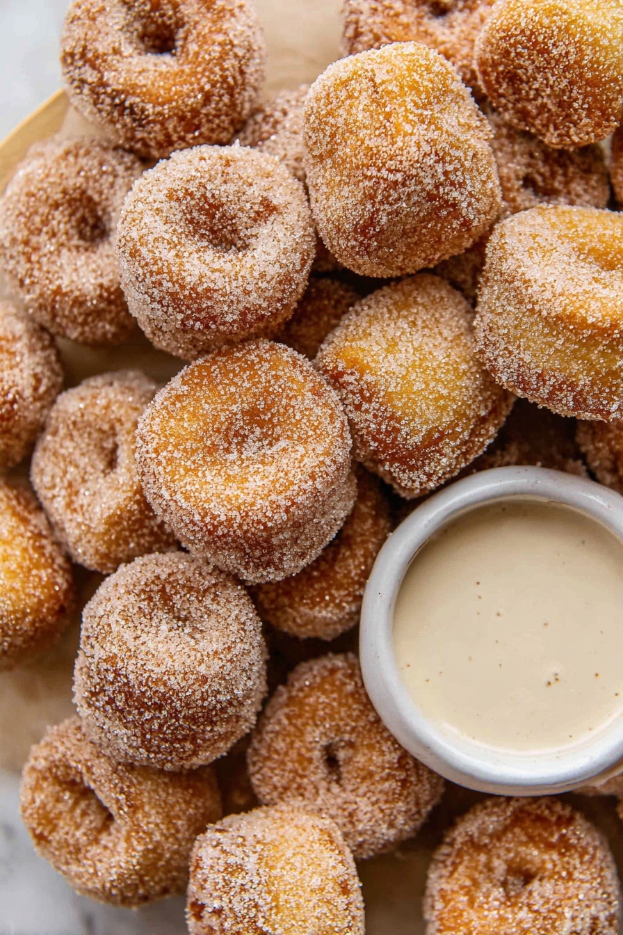 Cinnamon Sugar Pretzel Bites Recipe 6 The image shows many small, round donuts covered in sugar, piled closely together. The donuts have a golden-brown color with a rough sugar coating, giving them a sparkling look. In the center, there is a small, white bowl filled with a light creamy sauce. Everything is placed on a white marbled surface that adds a clean and bright background to the scene. The composition is close-up, focusing on the texture and color of the donuts and the bowl. photo taken with an iphone --ar 2:3 --v 7 - Cinnamon Sugar Pretzel Bites, Cinnamon Sugar Pretzel Snacks, Easy Cinnamon Pretzel Bites, Soft Cinnamon Sugar Bites, Quick Cinnamon Pretzels
