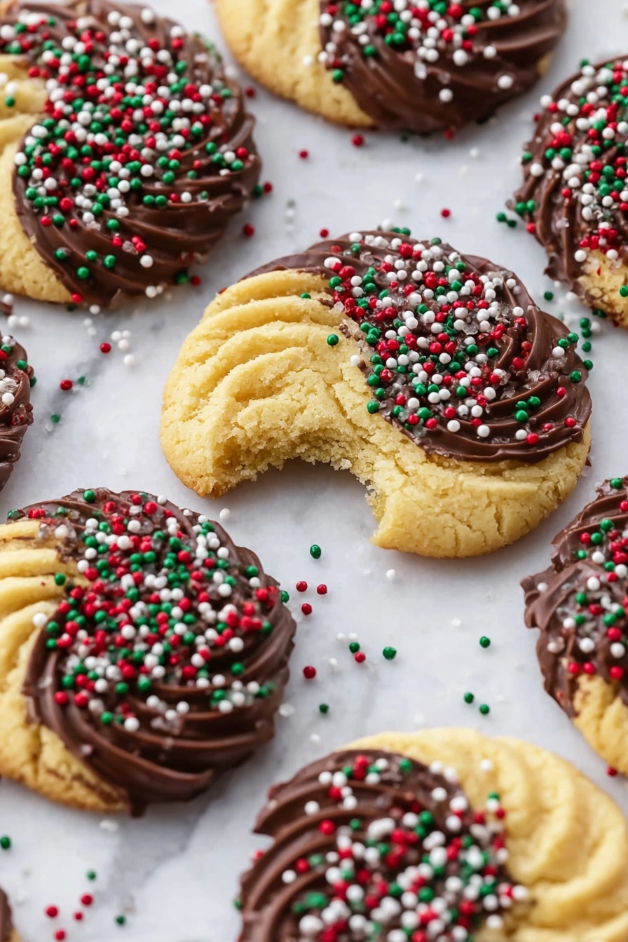 Danish Butter Cookies with Chocolate Chrome Recipe 6 The image shows several round cookies with a swirl pattern, each partially dipped in dark brown chocolate on one side, covered with small, round sprinkles in red, green, and white. The cookies are light golden yellow and have a crumbly texture, with one cookie in the center showing a bite taken from it. The cookies are placed evenly spaced on a white marbled surface. Some loose sprinkles are scattered around the cookies. Photo taken with an iphone --ar 2:3 --v 7 - Danish Butter Cookies with Chocolate Chrome, Danish butter cookies, chocolate coated cookies, festive holiday cookies, easy Danish cookie recipe