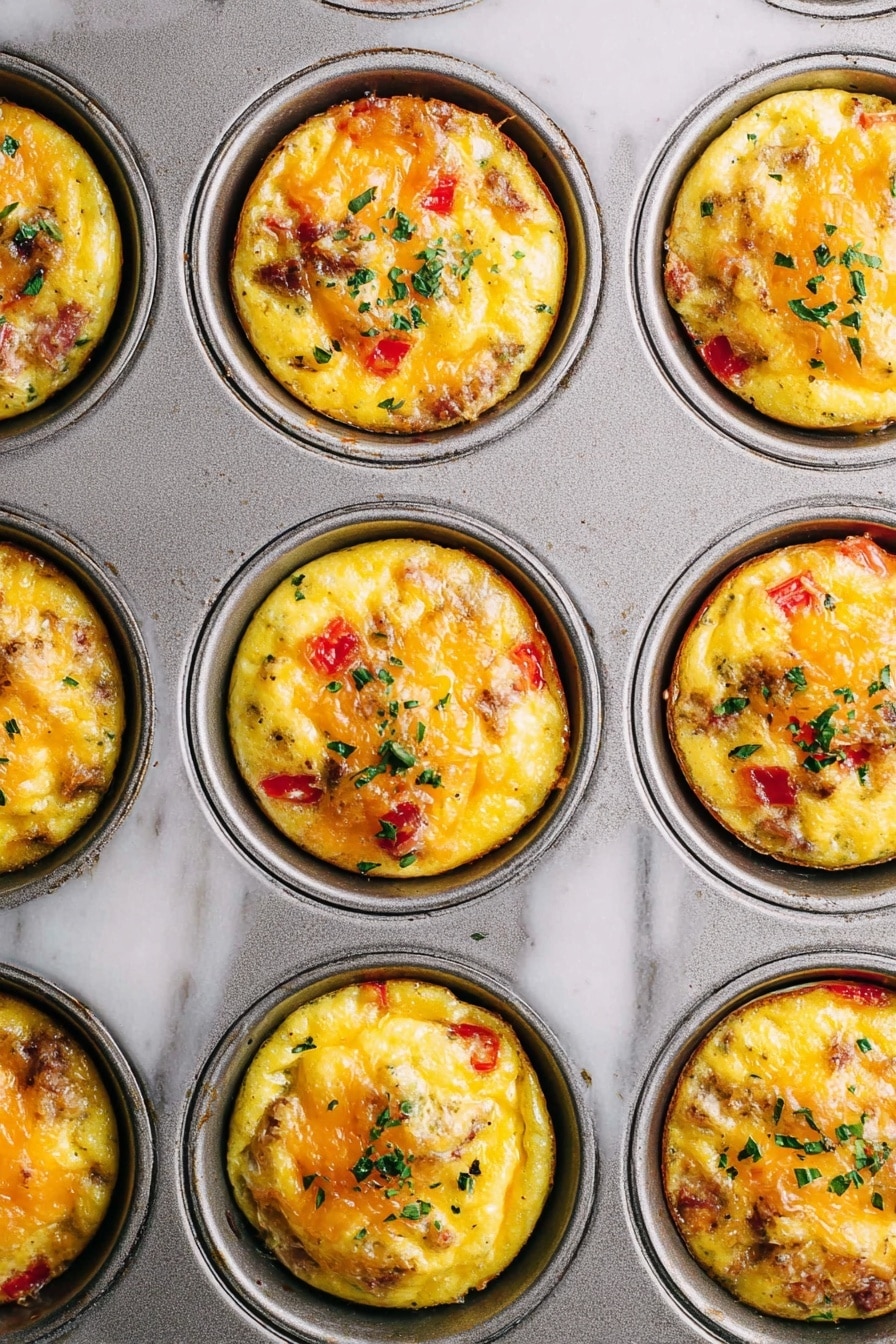 The image shows a close-up of a metal muffin tray filled with nine egg muffins. Each muffin has a golden yellow base with visible pieces of red bell pepper and bits of cooked meat mixed inside. The top surface of each muffin has melted cheese bubbling and slightly browned, with small green herb leaves sprinkled on them. The tray rests on a white marbled surface, showing slight texture and wear. The egg muffins sit neatly in each round muffin cup, with even and rounded tops, each garnished similarly with herbs. photo taken with an iphone --ar 2:3 --v 7 - Hash Brown Egg Cups, breakfast egg cups, easy breakfast recipes, make-ahead breakfast ideas, tasty brunch recipes