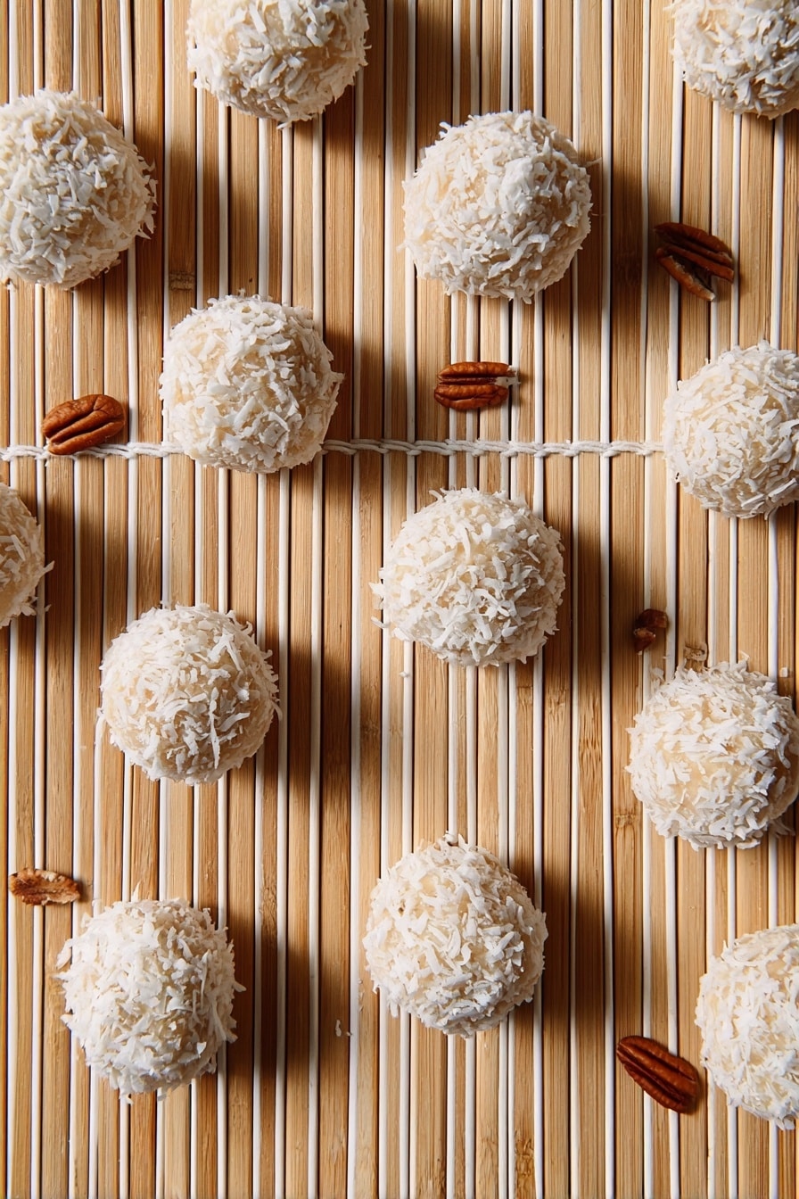 Orange Coconut Snowballs Recipe 6 The image shows multiple round balls covered with white coconut flakes arranged on a light bamboo matt with parallel white strings running vertically. The balls have a beige base visible through the coconut flakes and are scattered evenly across the frame. There are small pecan nuts placed randomly around the balls, adding a brown color contrast to the scene. The overall look is clean with a natural, textured feel. Photo taken with an iphone --ar 2:3 --v 7 - Orange Coconut Snowballs, tropical coconut treats, citrus dessert bites, easy holiday snacks, quick no-bake dessert
