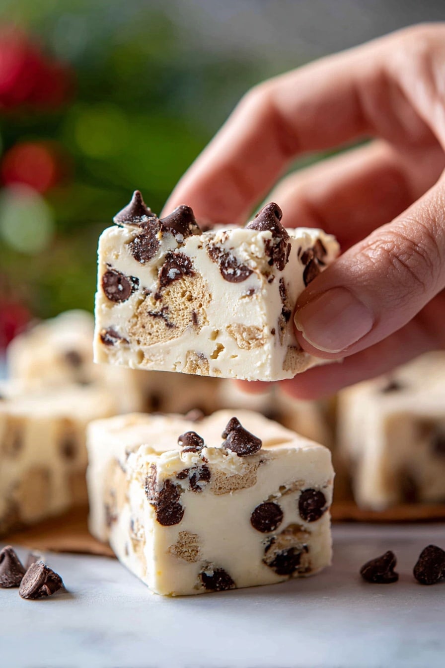 The image shows a pile of square white fudge pieces stacked on a white plate, placed on a white marbled surface. Each fudge piece has two main layers: a creamy white base layer with smooth texture and embedded tiny chocolate chips scattered inside, and a top layer with chunks of light brown cookie pieces and dark shiny chocolate chips unevenly spread on the surface. The fudge squares have a soft but firm look with slightly rough edges where they were separated. In the background, there is a blurred green pine branch and a brown pine cone. photo taken with an iphone --ar 2:3 --v 7 - Milk and Cookies Fudge, easy cookie fudge recipe, creamy cookie fudge, no-bake cookie fudge, festive cookie fudge dessert