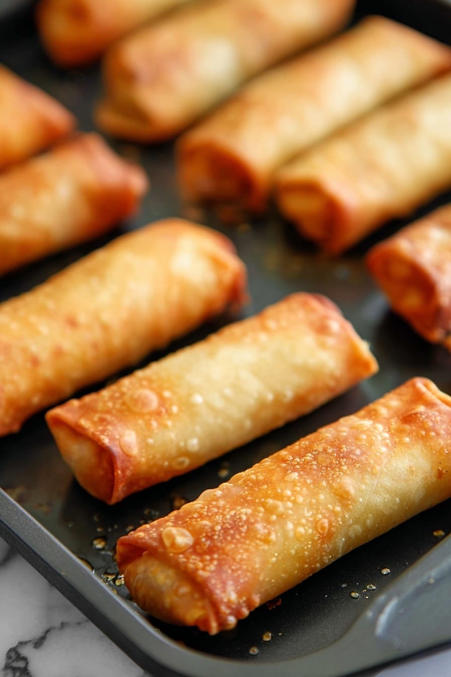 Crispy Oven Baked Egg Rolls Recipe 6 The image shows several golden brown egg rolls placed on a black baking tray with a few small spots of oil around them. Each egg roll is cylindrical with a crispy texture, highlighted by bubbles and slight browning on the surface. The edges are neatly rolled and sealed, showing a slight overlap of the thin dough layer. The egg rolls are arranged in rows, with three in the foreground sharply in focus, while the background rolls are slightly blurred. The whole scene is set on a white marbled surface. photo taken with an iphone --ar 2:3 --v 7 - Crispy Oven Baked Egg Rolls, healthy baked egg rolls, easy egg roll recipe, crunchy egg rolls without frying, baked veggie egg rolls