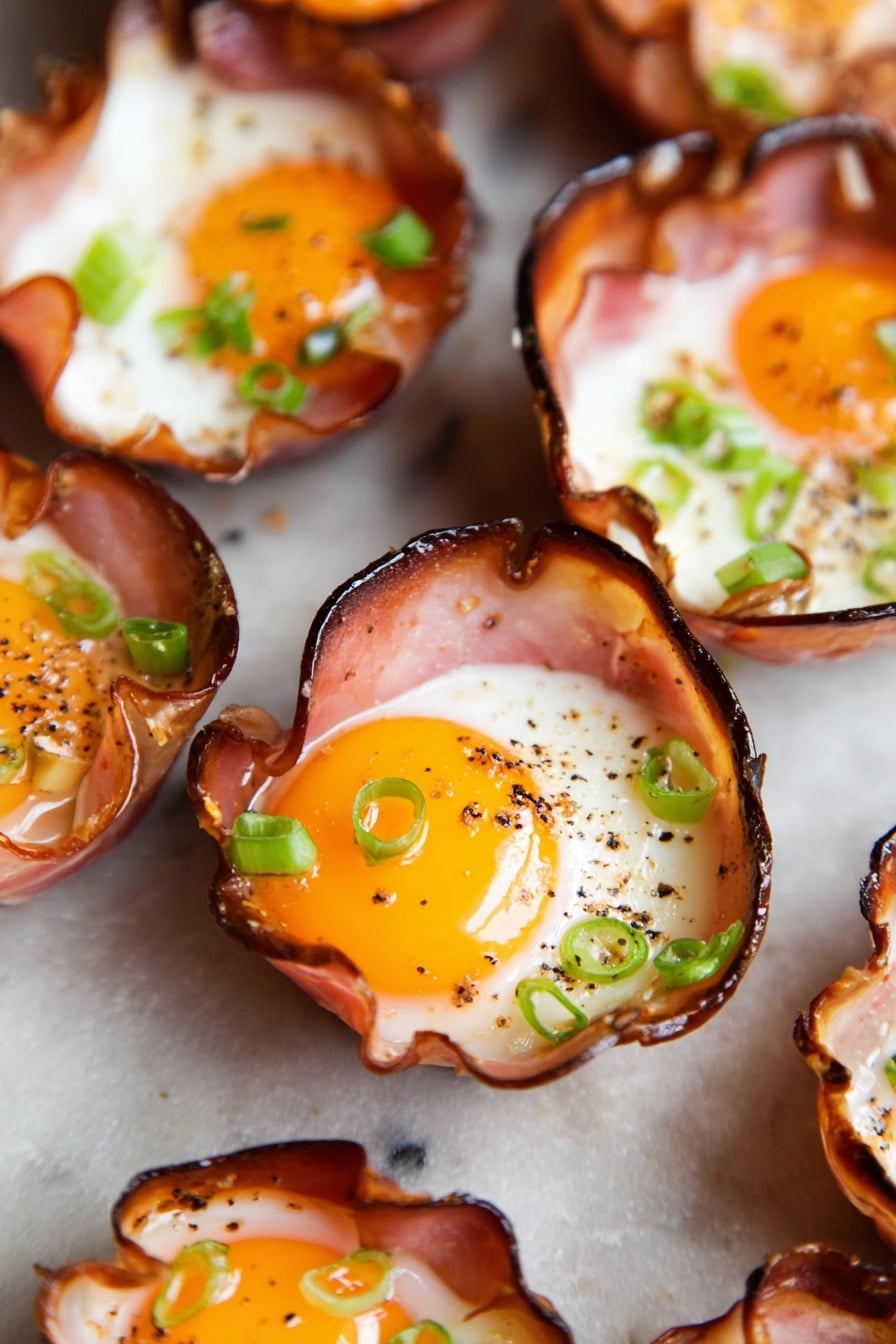 Ham and Cheese Egg Muffins Recipe 6 The image shows several small cups made from thin slices of cooked ham, each cup holding a cooked egg. Each egg has a bright yellow yolk in the center with white surrounding it. The edges of the ham cups are slightly crispy and darkened. Small green onion slices are scattered on top of the eggs for garnish, and there is some ground black pepper sprinkled over the yolks and whites. The cups are placed close together on a flat surface with a white marbled texture. photo taken with an iphone --ar 2:3 --v 7 - Ham and Cheese Egg Muffins, savory egg muffins with ham and cheese, quick breakfast ideas, easy egg muffin recipes, protein-packed breakfast bites
