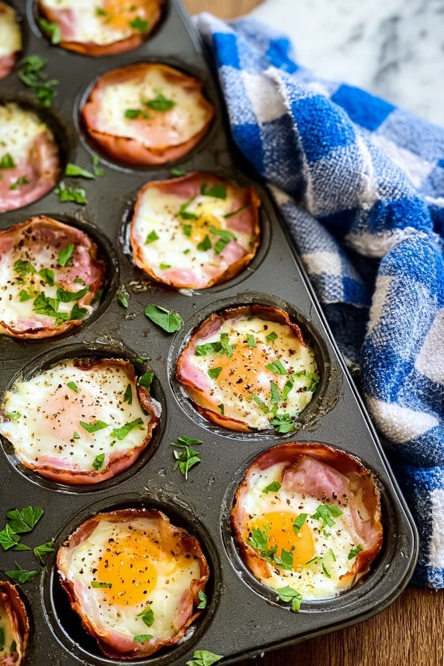 Ham and Egg Cups Recipe 6 The image shows a dark metal muffin tray filled with baked egg cups, each made with a layer of pinkish ham lining the cup, topped with cooked white eggs that have slightly browned edges and soft yellow yolks in the center, sprinkled with black pepper and small chopped green herbs. The egg cups are arranged in a 3 by 4 grid in the tray. The tray rests on a wooden surface with a blue and white checkered cloth draped nearby, and the background is a white marbled texture. Photo taken with an iphone --ar 2:3 --v 7 - Ham and Egg Cups, Ham and Egg Cups recipe, Breakfast Egg Cups, Easy breakfast muffins, protein-packed breakfast ideas