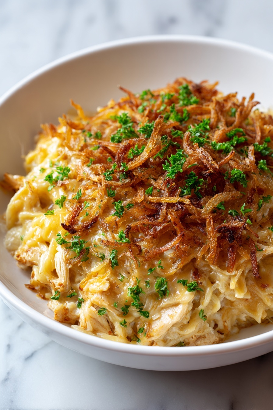 A white bowl holds a creamy, pale yellow noodle dish with three layers visible: the base layer of soft noodles mixed with chunks of chicken, the middle melted cheese layer that is slightly golden and stringy, and the top layer of crispy, dark golden-brown fried onions scattered all around. Small fresh green parsley pieces are sprinkled evenly on top, adding a bright contrast to the rich colors. The bowl sits on a white marbled surface with soft natural lighting. Photo taken with an iphone --ar 2:3 --v 7 - French Onion Chicken Orzo Bake, French Onion Chicken casserole, baked chicken and orzo with caramelized onion, savory chicken and orzo bake, comforting onion chicken casserole