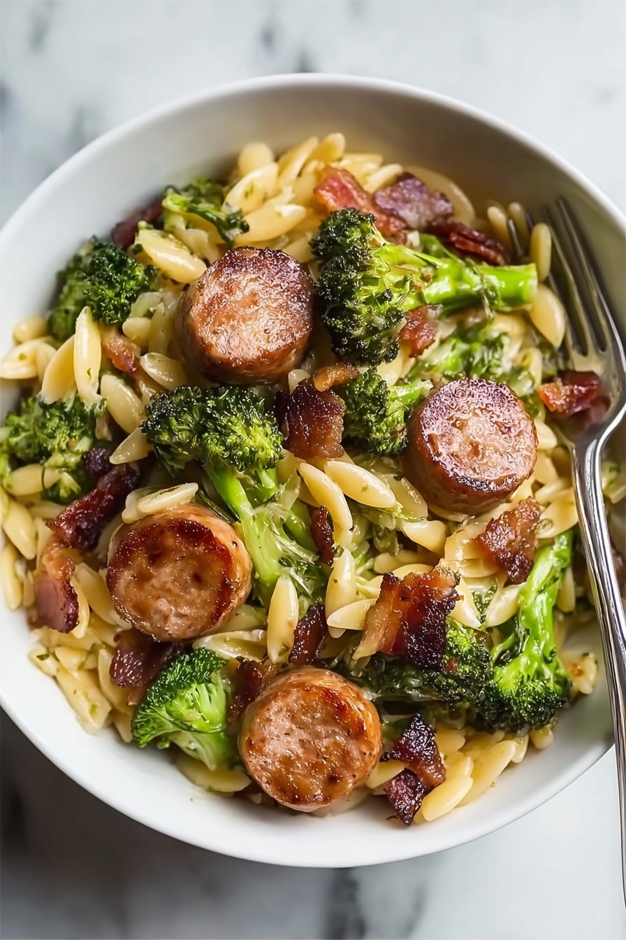 Chicken Sausage Broccoli Orzo Recipe 6 The dish is served in a white bowl on a white marbled surface. It has a base layer of small, oval-shaped pasta in a light yellow color. Scattered throughout and on top are green broccoli florets with a slightly rough texture. On top of these are several round slices of browned sausage with a crispy, golden-brown outer surface and a juicy interior. Small pieces of cooked bacon or similar meat are mixed in, adding dark reddish-brown spots throughout the dish. A fork is placed inside the bowl on the right side. Photo taken with an iphone --ar 2:3 --v 7 - Chicken Sausage Broccoli Orzo, healthy chicken sausage pasta, quick weeknight dinner recipes, easy broccoli orzo dish, one-pot chicken sausage meal