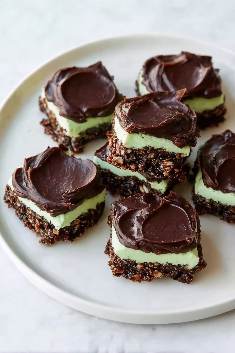 Fudgy Mint Chocolate No-Bake Cookies Recipe 8 The image shows a white plate with eight square-shaped treats arranged loosely on its surface, sitting on a white marbled background. Each treat has three distinct layers: a bottom layer made of a dark, chunky, chocolatey mixture with a rough texture, a middle thin layer of smooth light green cream, and a top thick layer of dark chocolate spread with a glossy, slightly uneven surface. The treats vary slightly in shape but mostly appear square with rounded edges. The lighting is bright and natural, highlighting the shiny top layer and the creamy middle layer. Photo taken with an iphone --ar 2:3 --v 7 - Fudgy Mint Chocolate No-Bake Cookies, mint chocolate dessert, no-bake chocolate cookies, quick mint fudge treats, easy summer dessert