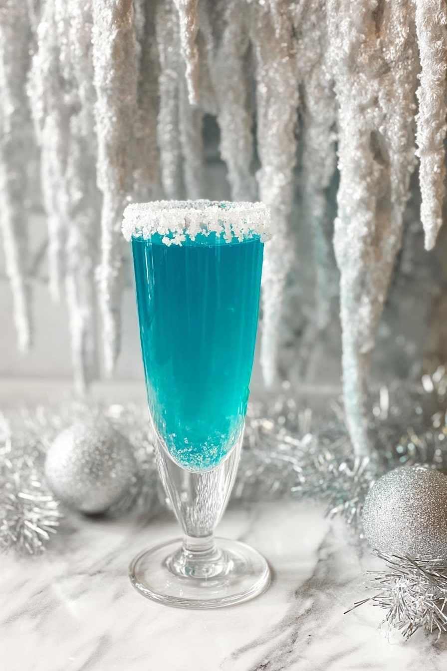 A tall clear glass filled with bright blue liquid, with a single layer of thick white sugar crystals rimmed around the top edge. The glass stands on a white marbled surface, surrounded by white shimmering tinsel. Behind the glass hangs a large decoration resembling white icicles with a glittery, icy texture, adding a frosty winter feel. The photo taken with an iphone --ar 2:3 --v 7 - Blue Curacao Champagne Mimosa, Blue Curacao cocktail, Champagne brunch drinks, Tropical mimosa recipe, Easy celebratory cocktails